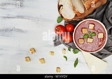 Calda zuppa di pomodoro con formaggio parmigiano e le foglie di basilico con crostini. Immagine ripresa da sopra al piatto stile di laici. Foto Stock