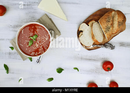 Calda zuppa di pomodoro con foglie di basilico e parmigiano, di pomodori freschi e di un filone di erborinati crosta di pane. Immagine ripresa da sopra al piatto stile di laici. Foto Stock