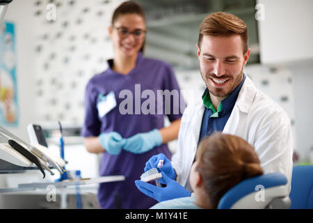 Sorridente dentista mostra correttamente la spazzolatura dei denti sul modello di denti nella mascella di paziente giovane Foto Stock