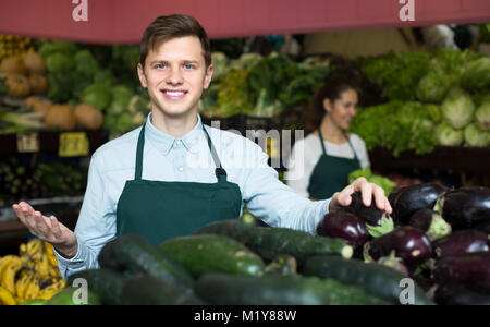 Sorridente roba europea nel grembiule verde vendita cetriolo al marketplace Foto Stock