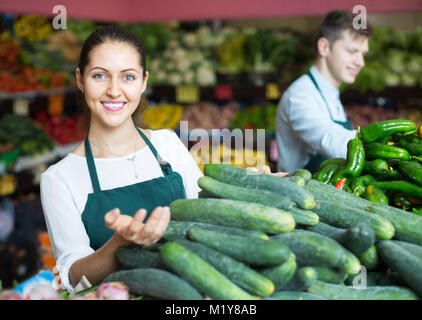 Felice roba russa nel grembiule verde vendita cetriolo al marketplace Foto Stock