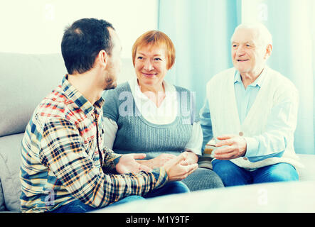 Il nonno e la nonna conversazione calorosamente con il nipote a casa sul lettino Foto Stock