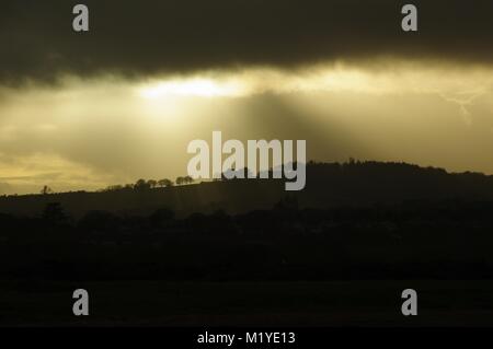 La luce del tramonto d'oro e Sunray da cova infausto Stratus Rainclouds sopra una collina profilarsi. Dawlish Warren, South Devon, Regno Unito. L'inverno 2016. Foto Stock