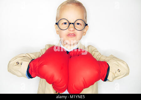 Little Boy in bicchieri e guantoni da pugilato cercando in modo aggressivo in telecamera su sfondo per studio. Foto Stock