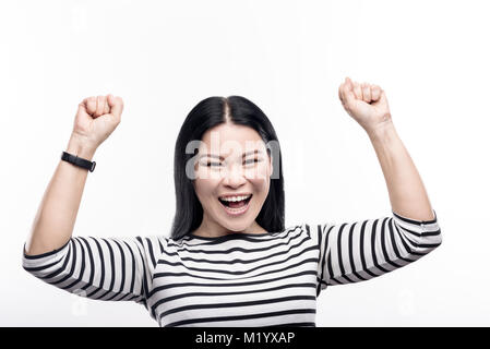 Carino dai capelli scuri donna alzando le mani gioiosamente Foto Stock