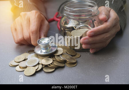 Uno stetoscopio con monete in vaso con denaro stack, concetto finanziario, contabile, di business e di investimenti di risparmio. Foto Stock