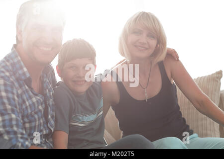 I genitori e il loro figlio sedersi rannicchiato nella stanza vivente e sorridente Foto Stock