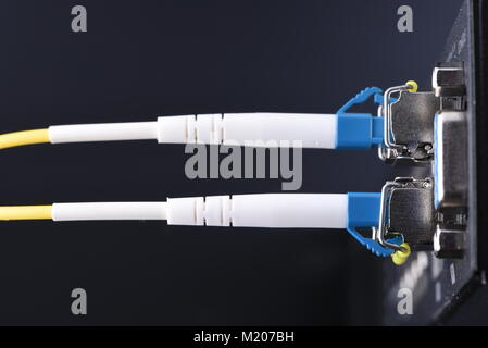 Dispositivi di rete tecnologia, cavo in fibra ottica e interruttore, close-up su sfondo nero Foto Stock