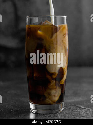 Iced caffè nero con ghiaccio e latte versando in Foto Stock