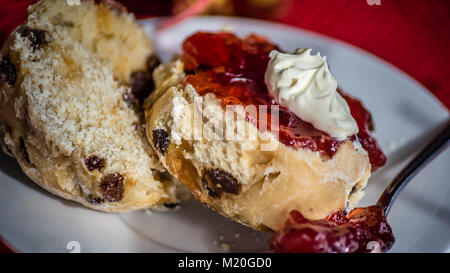 Cornetto con panna montata e confettura di fragole, cibo macro, il fuoco selettivo. Il tè del pomeriggio, la pasta sulla piastra bianca sfondo rosso, chiave di basso. Foto Stock