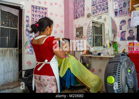 Tulum, Quintana Roo, Messico, donna messicana che taglia i capelli del cliente in un barbiere Foto Stock