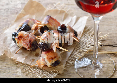 Deliziose tapas spagnole: fritto prugne avvolto in pancetta servita portoghese con il vino di porto Foto Stock