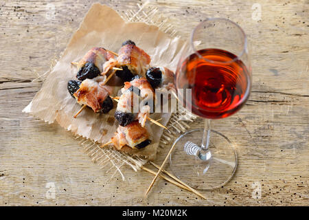 Deliziose tapas spagnole: fritto prugne avvolto in pancetta servita portoghese con il vino di porto Foto Stock