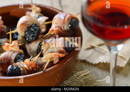 Deliziose tapas spagnole: fritto prugne avvolto in pancetta servita portoghese con il vino di porto Foto Stock