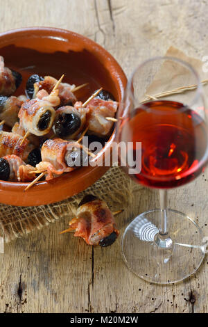 Deliziose tapas spagnole: fritto prugne avvolto in pancetta servita portoghese con il vino di porto Foto Stock