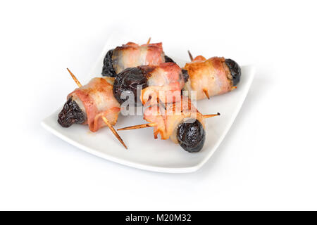 Deliziose tapas spagnole su sfondo bianco: fritto prugne avvolto in pancetta Foto Stock