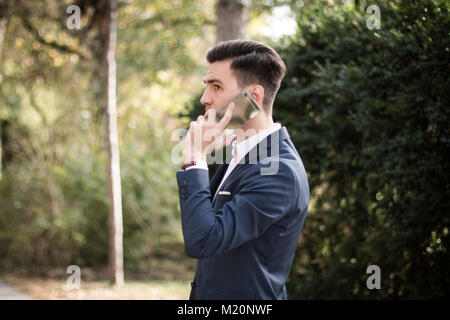 Elegante giovane uomo con lo smartphone all'aperto in un parco. Avere una conversazione telefonica. Foto Stock