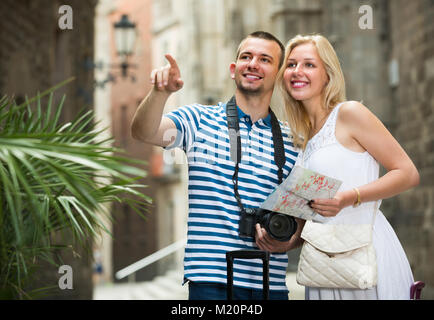Ritratto di felice coppia turisti tenendo a piedi e trascinando valigie in città il giorno di estate Foto Stock
