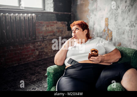 Grasso donna si siede su una sedia e mangia caramelle, sovrappeso. Uno stile di vita poco salutare, obesità Foto Stock