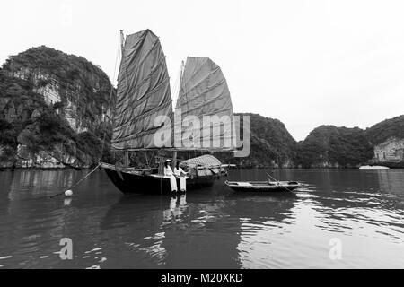 Due giovani donne vietnamita in posa sul bordo di un sampan, una tradizionale barca a vela nella Baia di Halong, Vietnam. Che indossano il tipico Ao IAM e Non La. Foto Stock