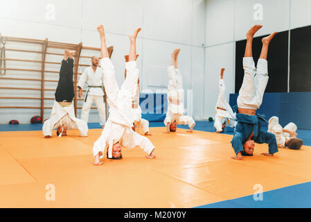 Bambini karate, kids in kimono pratica delle arti marziali di hall. Bambini e bambine in uniforme su sport training, capovolto esercizio Foto Stock