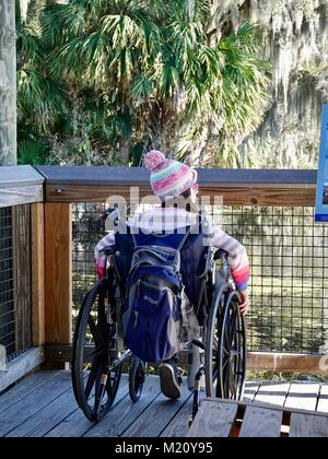 Ragazza seduta in sedia a rotelle e per godersi la natura, sul lungomare di Paynes Prairie preservare parco statale, Gainesville, Florida, Stati Uniti d'America. Foto Stock