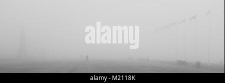 Un bambino cavalca la sua bicicletta attraversando il lungomare su Plymouth Hoe nella fitta nebbia. Una statua di Drake, pennoni e altre persone possono solo essere effettuata. Foto Stock