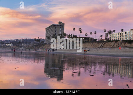 Il Tourist Hotel Resort a San Diego, California, si riflette nella bassa sabbia da surf e nella gente che cammina sulla Pacific Beach durante il tramonto invernale Foto Stock