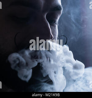 Uomo con la barba e Mustages Vaping una sigaretta elettronica. Tanga Vaper vaporizzatore di fumo e il fumo Exhals flusso dal naso. Foto Stock