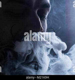 Uomo con la barba e Mustages Vaping una sigaretta elettronica. Tanga Vaper vaporizzatore di fumo e il fumo Exhals flusso dal naso. Foto Stock