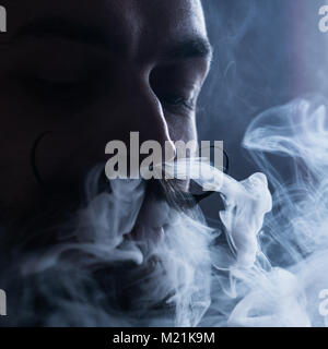 Uomo con la barba e Mustages Vaping una sigaretta elettronica. Tanga Vaper vaporizzatore di fumo e il fumo Exhals flusso dal naso. Foto Stock