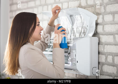 Sorridente giovane donna Pulizia del condizionatore d'aria con la bottiglia spray Foto Stock
