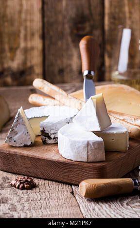 Scheda con diversi tipi di formaggio su tavola in legno rustico Foto Stock