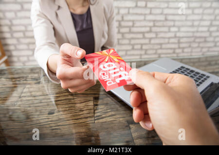 Close-up di una persona dando carta regalo per imprenditrice al lavoro in ufficio Foto Stock