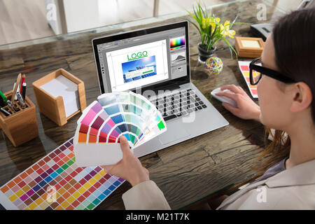 Una donna che mantiene i campioni di colore utilizzando un computer portatile con il Logo Design Software sullo schermo Foto Stock