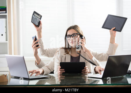Occupato giovane imprenditrice sorridente con sei bracci facendo diversi tipo di lavoro in ufficio Foto Stock