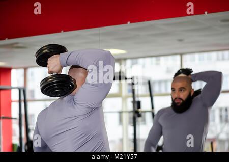 Forte atleta maschio il sollevamento pesi, guardando i risultati della sessione in specchio Foto Stock