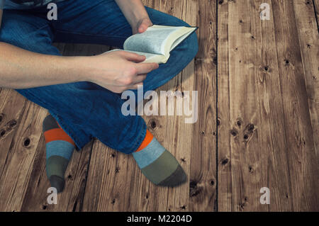 Donna seduta su un pavimento in legno e la lettura di un libro. Istruzione e concetto di relax Foto Stock