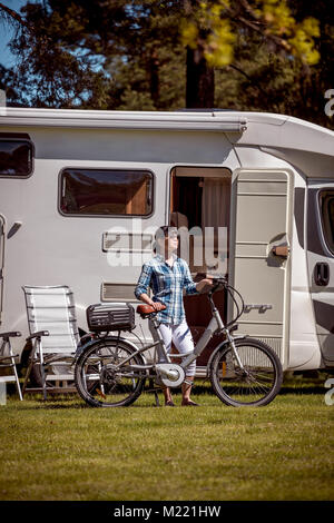 Donna sulla bicicletta elettrica in appoggio al campeggio. Vacanza per la famiglia in viaggio, viaggio vacanza in camper, caravan VR auto vacanza. Foto Stock