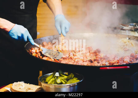 Chef di cucina salsicce stufato nel wok ampio presso la strada della citta'. Close-up del processo di cottura. Cucina di strada. La cucina nazionale Foto Stock