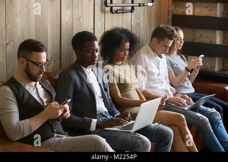 Multirazziale in bianco e nero la gente seduta sul lettino usando il dispositivo Foto Stock