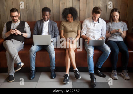 Multiculturale di giovani utilizzando computer portatili e smartphone seduta Foto Stock