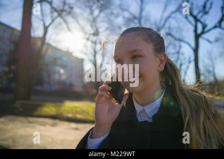 Teen ragazza camminare in città e parlare al telefono in giornata di primavera Foto Stock