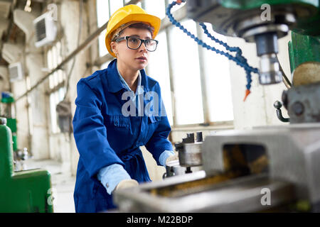 Ritratto di giovane moderno donna che indossa hardhat e uniforme di macchina operatrice unità a impianto moderno spazio di copia Foto Stock