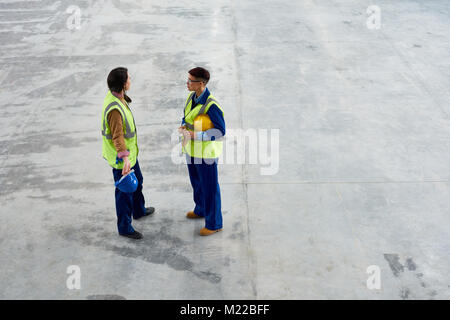 Angolo alto ritratto di due moderni giovani donne che lavorano presso la fabbrica di parlarsi in piedi grandi workshop, spazio di copia Foto Stock