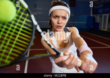 Ritratto di donna forte giocando a tennis nella corte interna, accigliata con il ceppo mentre si colpisce la palla con racket , girato con flash Foto Stock