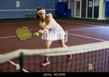 A piena lunghezza ritratto di donna forte giocando a tennis nella corte interna, accigliata con il ceppo mentre si colpisce la palla con racchetta, spazio di copia Foto Stock