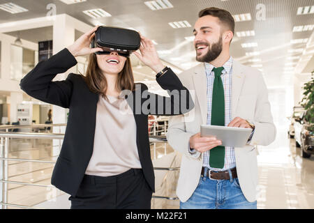 Ritratto della moderna giovane donna cercando sul casco VR in mall e guardando eccitato Foto Stock