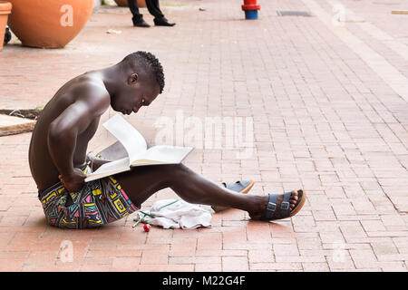 Cartagena, Colombia - Gennaio 23th, 2018: un giovane afro american colombiano uomo seduto sulla strada, guardando le pagine bianche di un notebook presso il Plaza Foto Stock