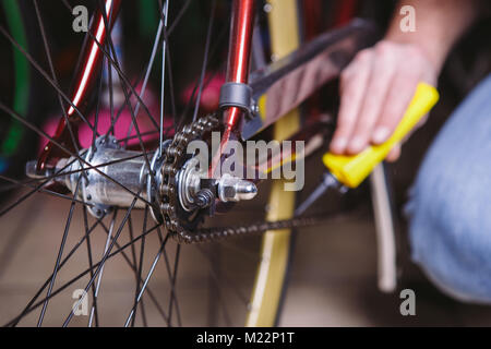 Tema la riparazione di biciclette. Close-up di un uomo caucasico la mano utilizzare un lubrificante per catena in un lubrificatore giallo per llubricator una catena di bicicletta su una bicicletta rossa. Foto Stock